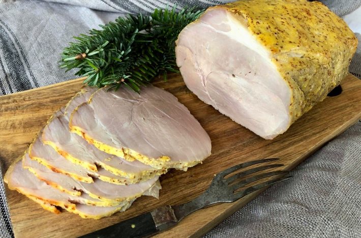 Uppskuren senapsgriljerad julskinka på ett träfat