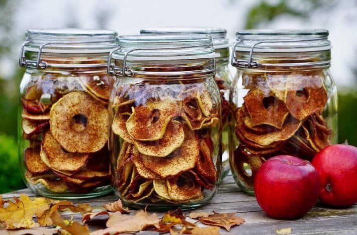 Torkade äppelringar i glasburkar med höstlöv och äppleringar bredvid