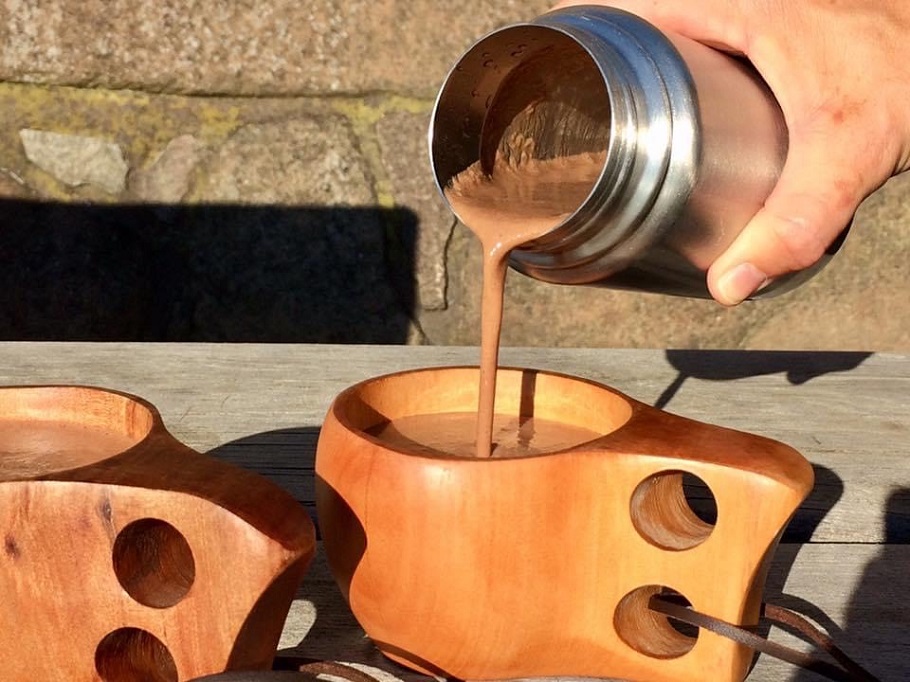 Häller upp varm choklad från en termos ner i en träkåsa